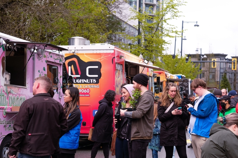 Mixed crowd, some holding plants others looking at phones wait for order at food truck