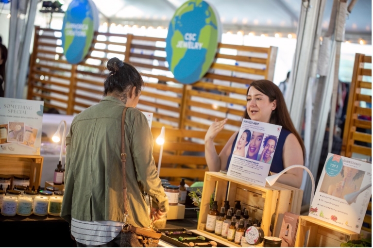 Market vendor talks to woman who is browsing the products on sale.