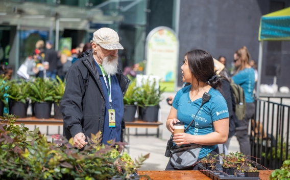 Man and young women in conversation next to table with plants for sale
