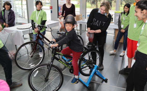 Child pedalling on a stationary bike that has been set up to power a blender to make smoothies