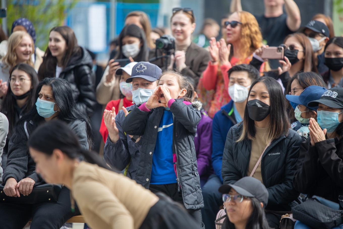 Young girl in midst of diverse crowds enthusiastically cheers on performers