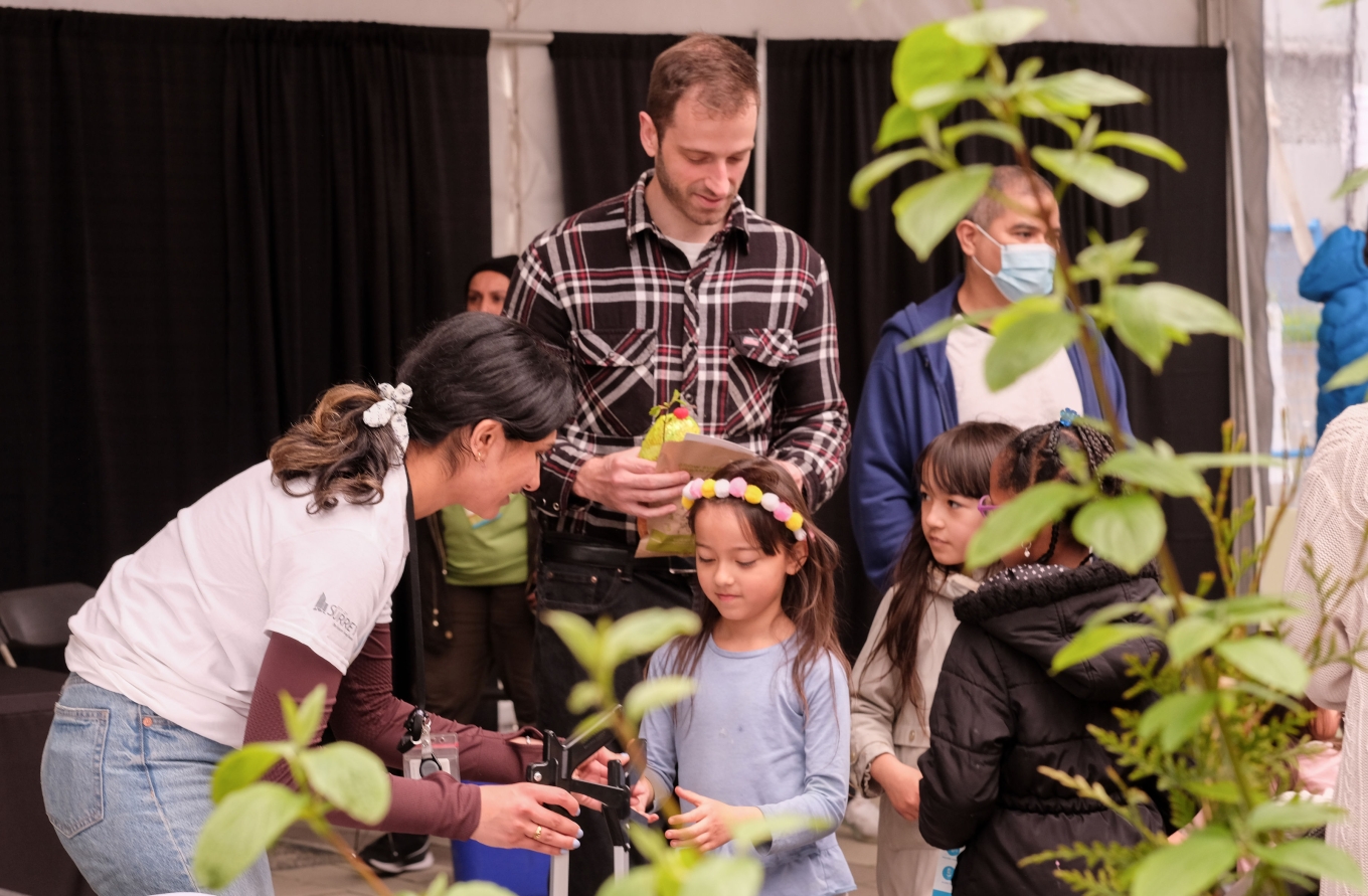 Three young girls and dad are engaged with exhibitor doing hands on demo